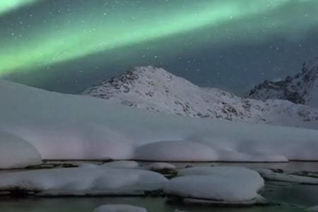 Northern Lights over snow-covered mountains and an icy river
