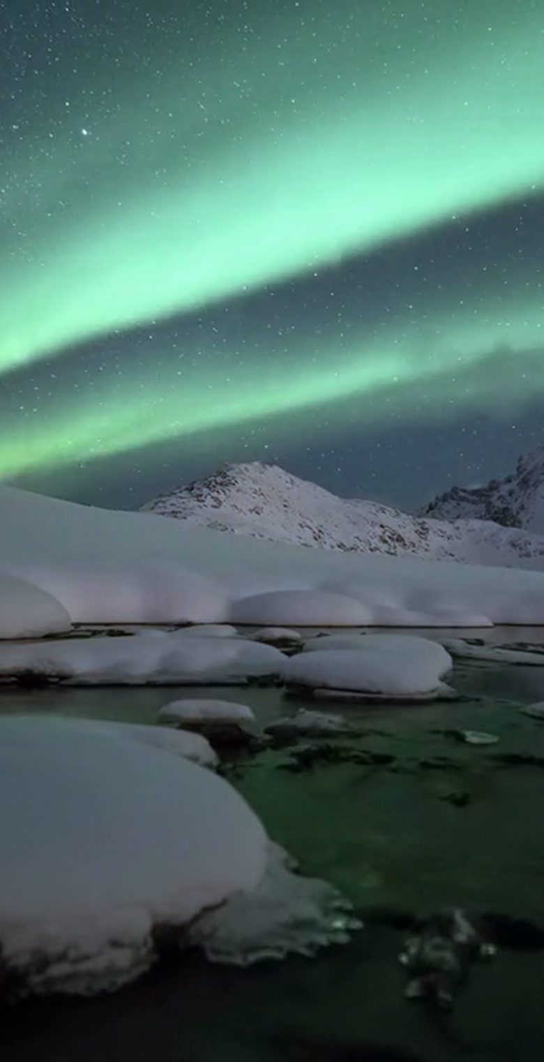 Northern Lights over snow-covered mountains and an icy river