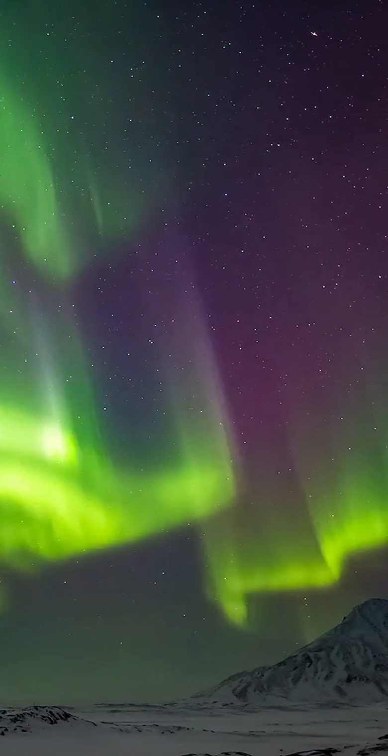 Green and purple Northern Lights above a snow-covered mountain